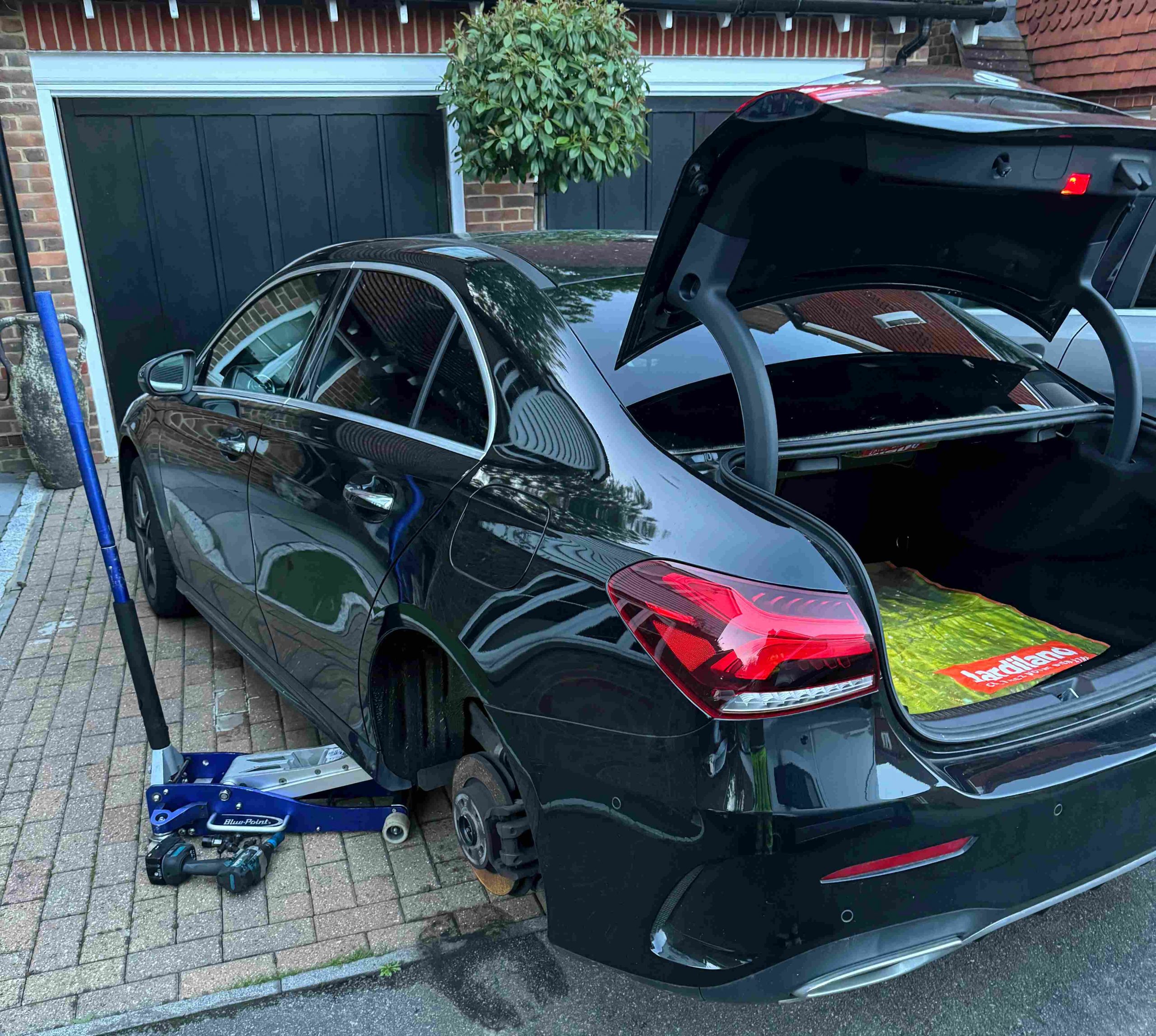 Black saloon car with a wheel off on a jack and the boot open, after locking wheel nut removal in King's Lynn